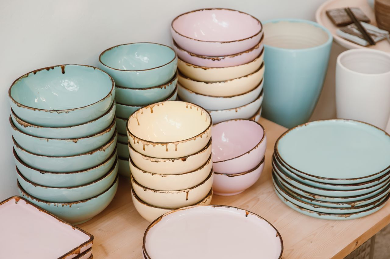 our-story-02 Pastel-colored ceramic bowls and plates neatly stacked on a wooden surface, showcasing rustic elegance.